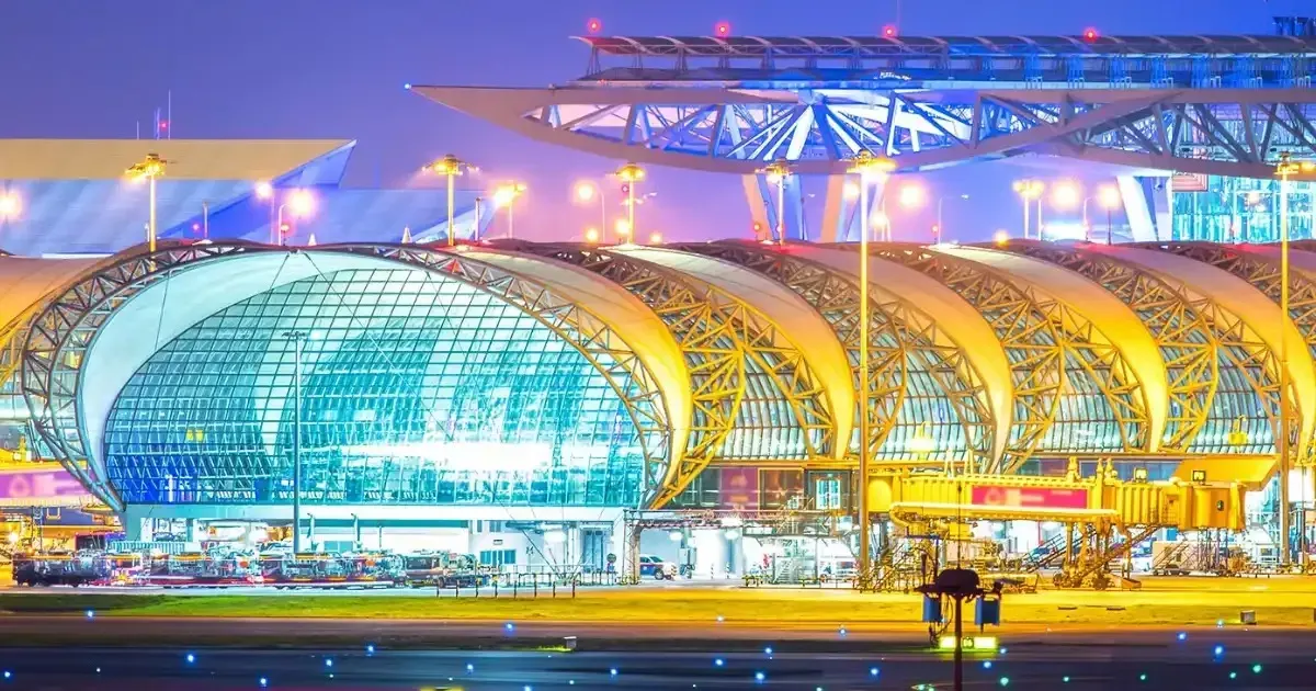Suvarnabhumi Airport terminal in Bangkok at dusk, its curved glass and steel roof lit from inside